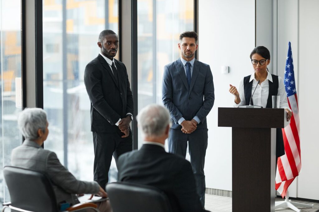 Three federal agents speaking at a podium with an American flag behind them, as part of their federal agency communication strategy.