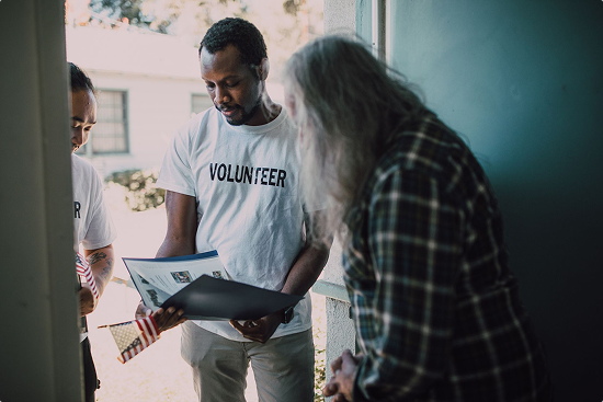 Two volunteers canvassing their neighborhood, holding American flags and showing a small binder of a public works project to someone at the door, as part of public consultation software guiding the process